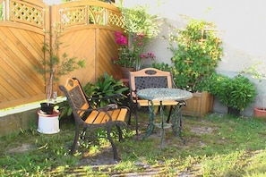 Eine Terrasse mit Holzzaun, einem kleinen Tisch, zwei Stühlen und Topfpflanzen.