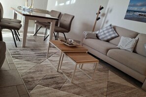 A living room with a sofa, a coffee table, and a dining area with chairs and a table. - Hahnenhof Apartment 7 (Wrixum)