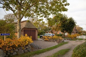 Een landweg naar een huis met een garage met rieten dak en een stenen muur.