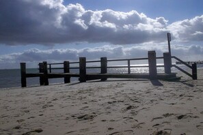 A beach with a wooden walkway leading to the water, a cloudy sky, and a calm sea. - Hahnenhof Apartment 7 (Wrixum)