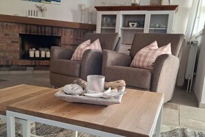 A cozy living room with a fireplace, two armchairs, a wooden coffee table, and a tray with decorative items. - Hahnenhof Apartment 7 (Wrixum)