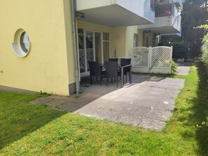 Een woongebouw met een terras, tuinmeubilair en een witte latten hek.