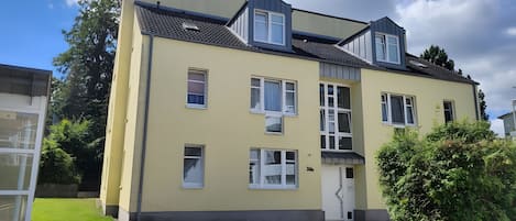 A multi-story residential building with a flat roof, multiple windows, and a visible entrance.