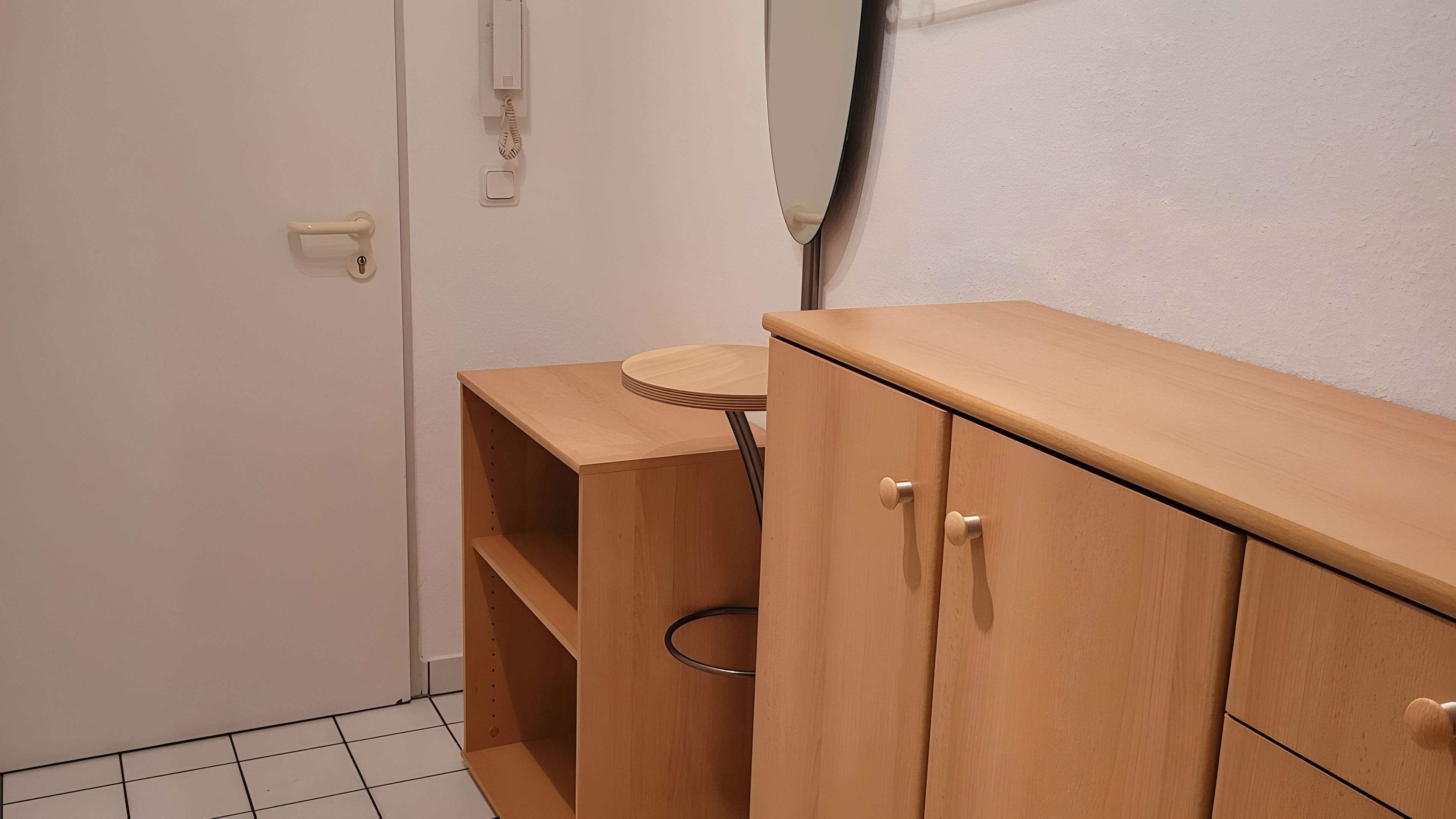 Ein Zimmer mit einem Holzschrank, einem kleinen Tisch und einer Tür mit Lichtschalter und Telefon.