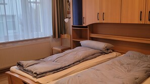 Een slaapkamer met twee bedden, een stoel, een plank en een raam met gordijnen.