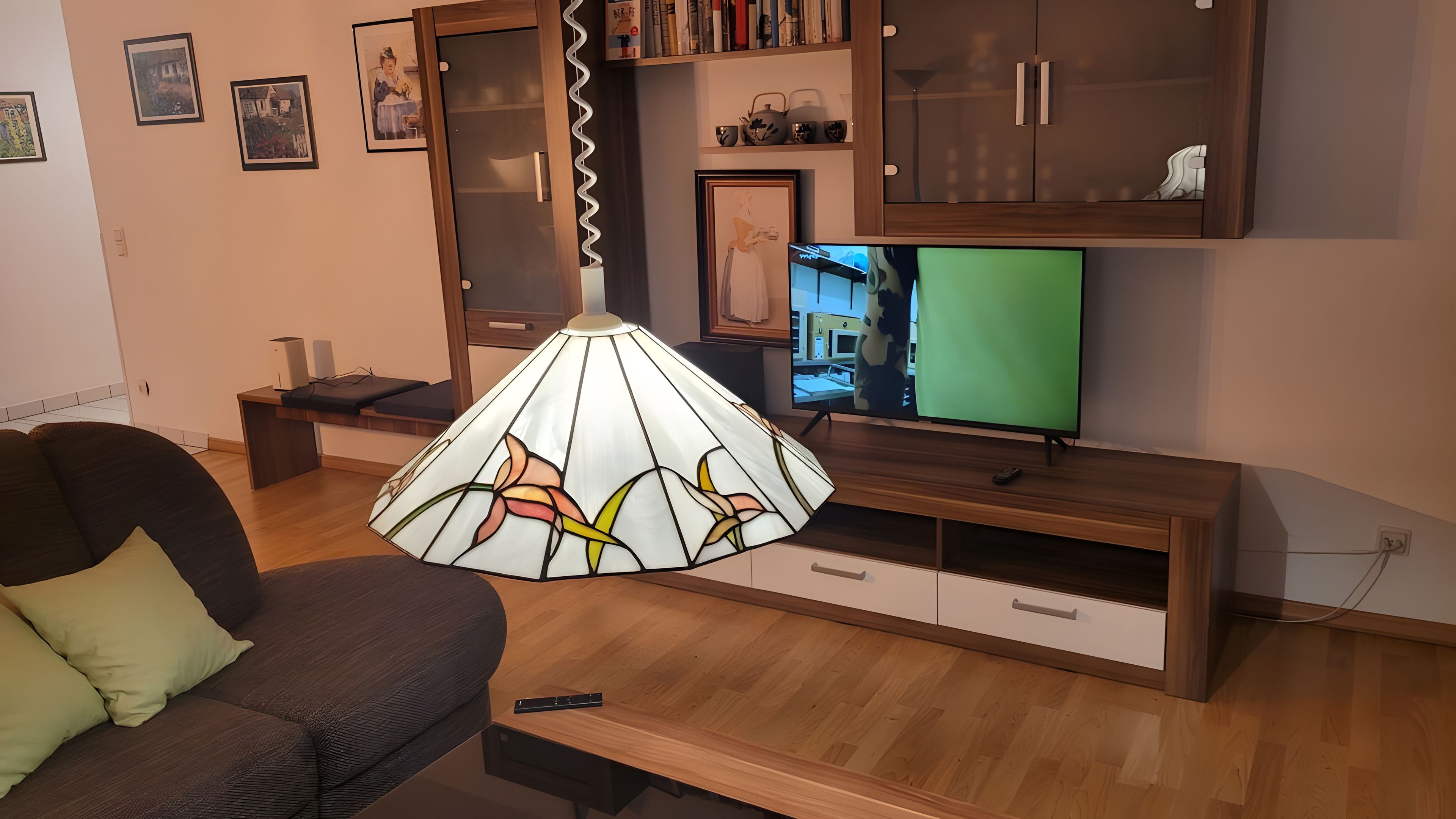 Ein Wohnzimmer mit einer Couch, einer Lampe, einem Fernseher und einem Holzschrank.