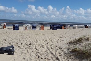 Une plage avec des cabanes de plage numérotées et une paire de sandales noires sur le sable.