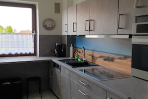Eine moderne Küche mit integriertem Geschirrspüler, einer Kaffeemaschine und Blick zum Strand durch ein Fenster.