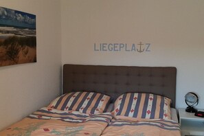 Une chambre à coucher avec un lit, des oreillers à rayures, une table de chevet avec une horloge et un tableau accroché au mur.