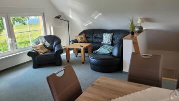 Een moderne woonkamer met een leren bank, een houten salontafel en een eettafel met stoelen.