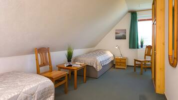 Quarto com cama, cadeira, mesa de cabeceira, mesa e janela com cortinas.