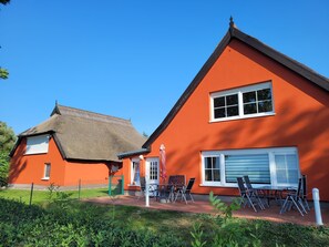 En tvåvåningsbyggnad med en röd fasad, ett halmtak och en liten veranda med utomhusmöbler.