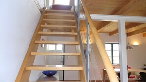 A wooden staircase leading to a lower level with a white wall and a blue bowl on the landing.