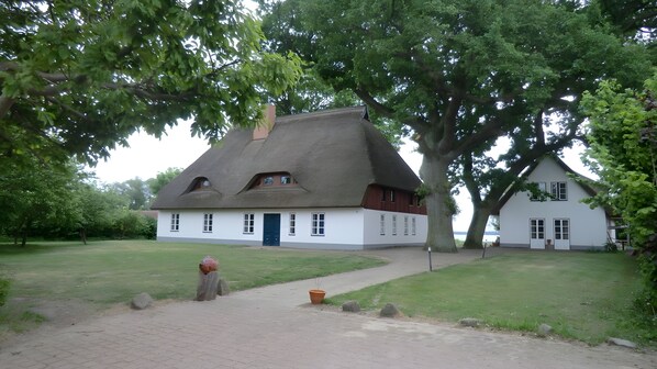 A traditional house with a thatched roof, surrounded by a well-maintained lawn and large trees.