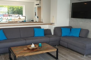 Ein modernes Wohnzimmer mit einer Eckcouch, einem Couchtisch und einem großen Fenster mit Blick auf die Straße.