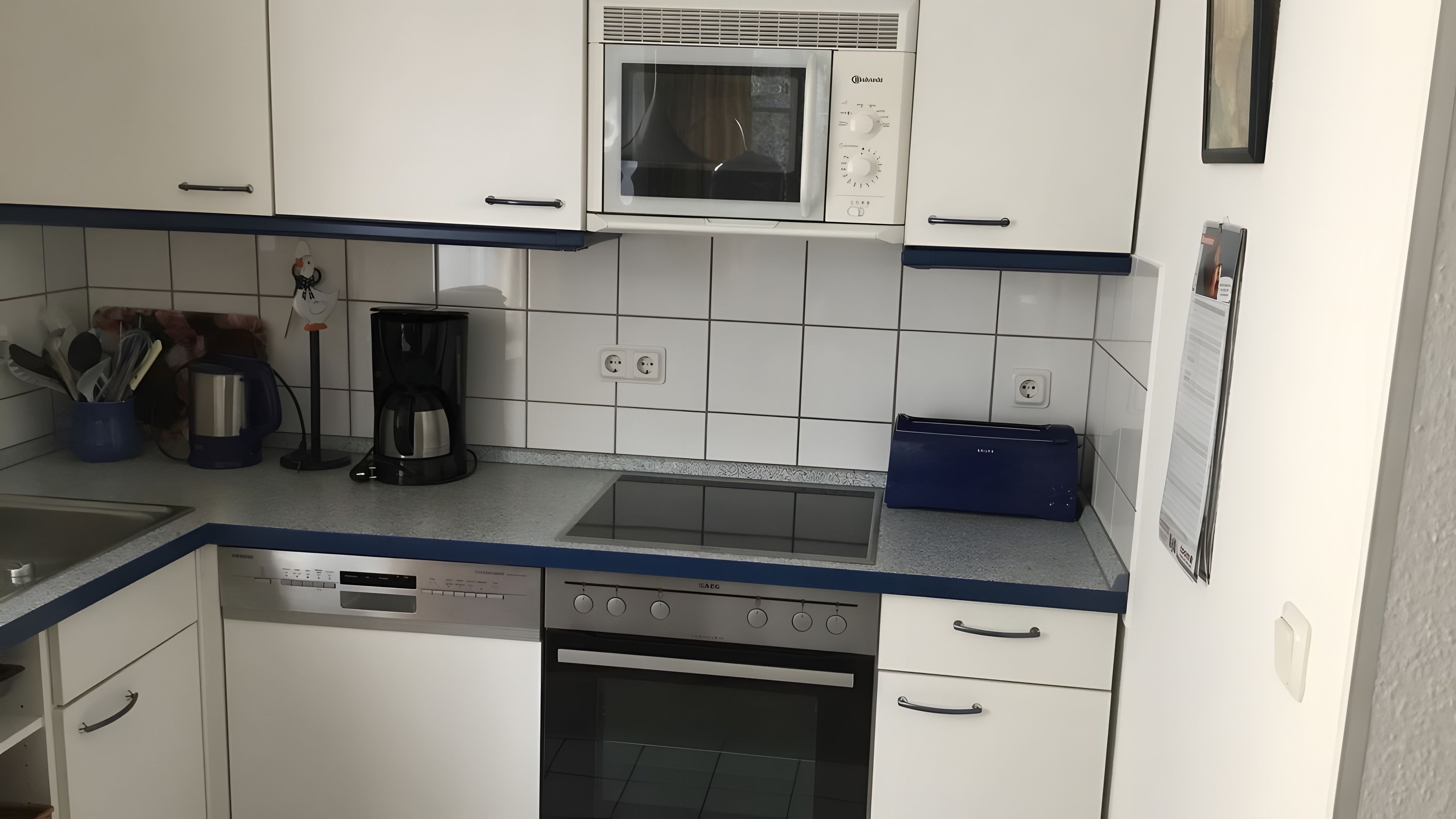 Una cocina con armarios blancos, microondas, cafetera, lavavajillas y estufa.