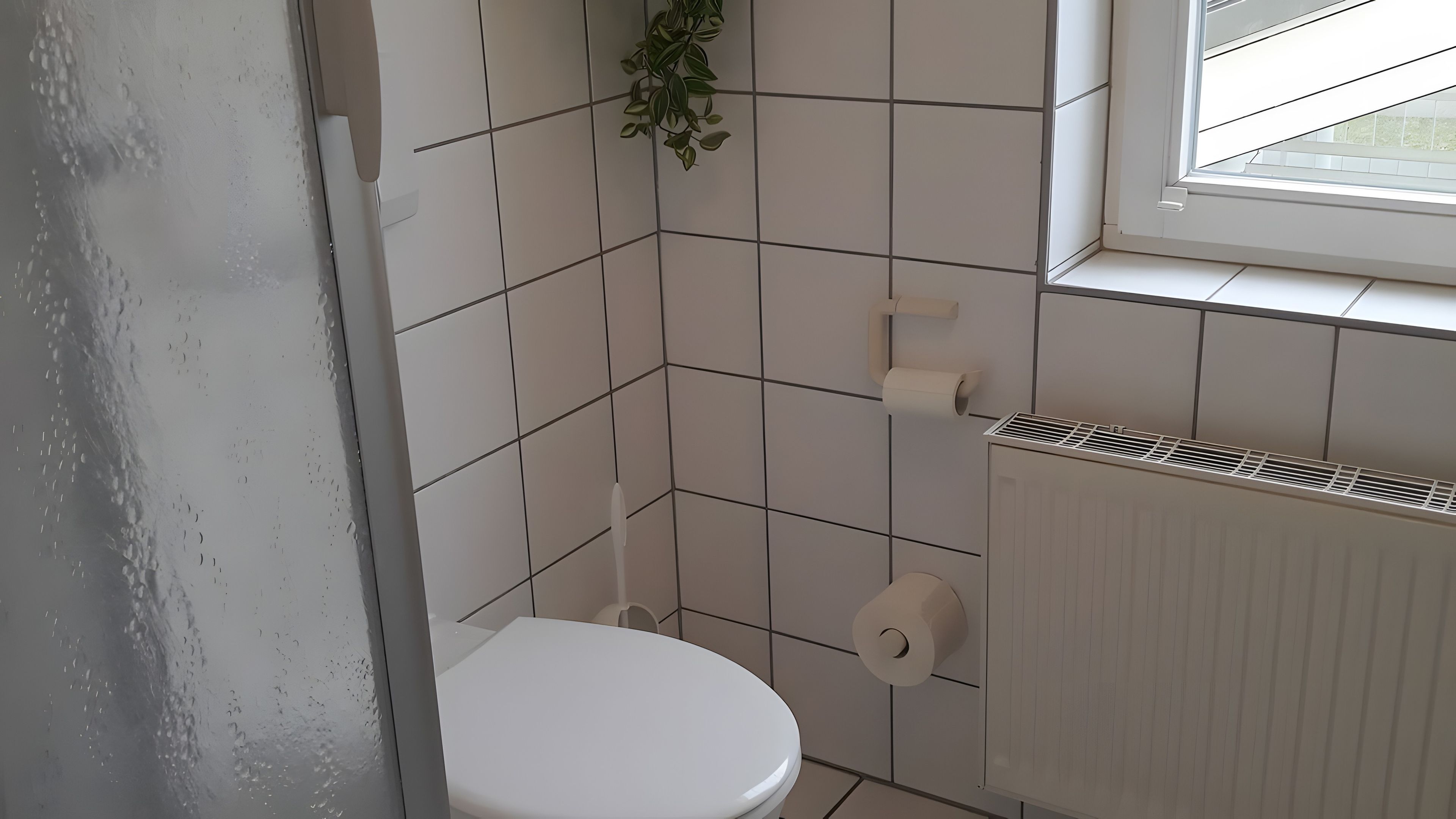 Ein kleines Badezimmer mit Fliesen, einer Toilette, einem Heizkörper und einem Fenster.