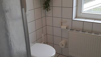 Ein kleines Badezimmer mit Fliesen, einer Toilette, einem Heizkörper und einem Fenster.