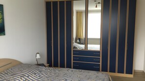 Ein Schlafzimmer mit einem Bett, einer Nachttischlampe, einem Kleiderschrank mit mehreren Schubladen und einem Spiegel.