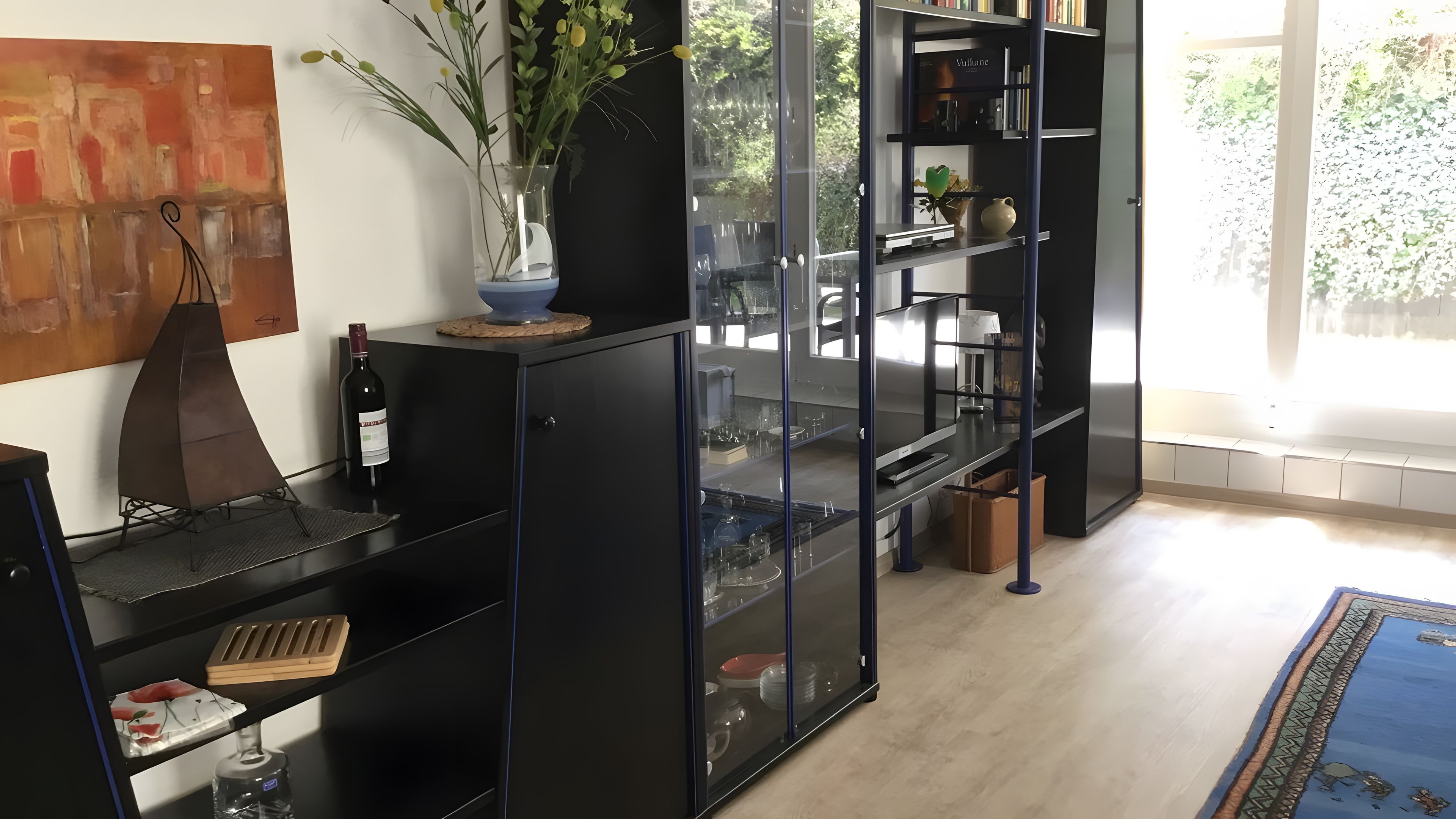 Ein modernes Interieur mit einem schwarzen Bücherregal, einer Weinflasche und einer Pflanzvase.