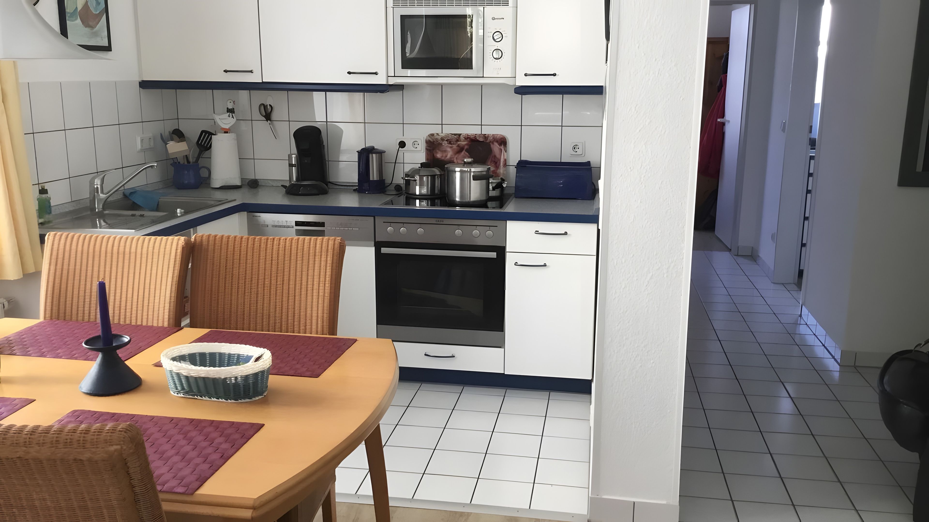 Eine kompakte Küche mit weißen Schränken, einer Mikrowelle, einem Backofen und einer Kaffeemaschine.