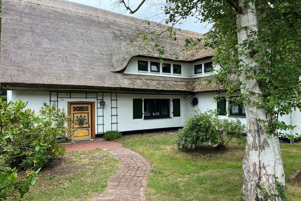 A traditional house with a thatched roof, a brick pathway leading to the entrance, and a well-maintained garden.