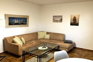 Ein Wohnzimmer mit einem braunen Sofa, einem Glastisch und drei gerahmten Bildern an der Wand.