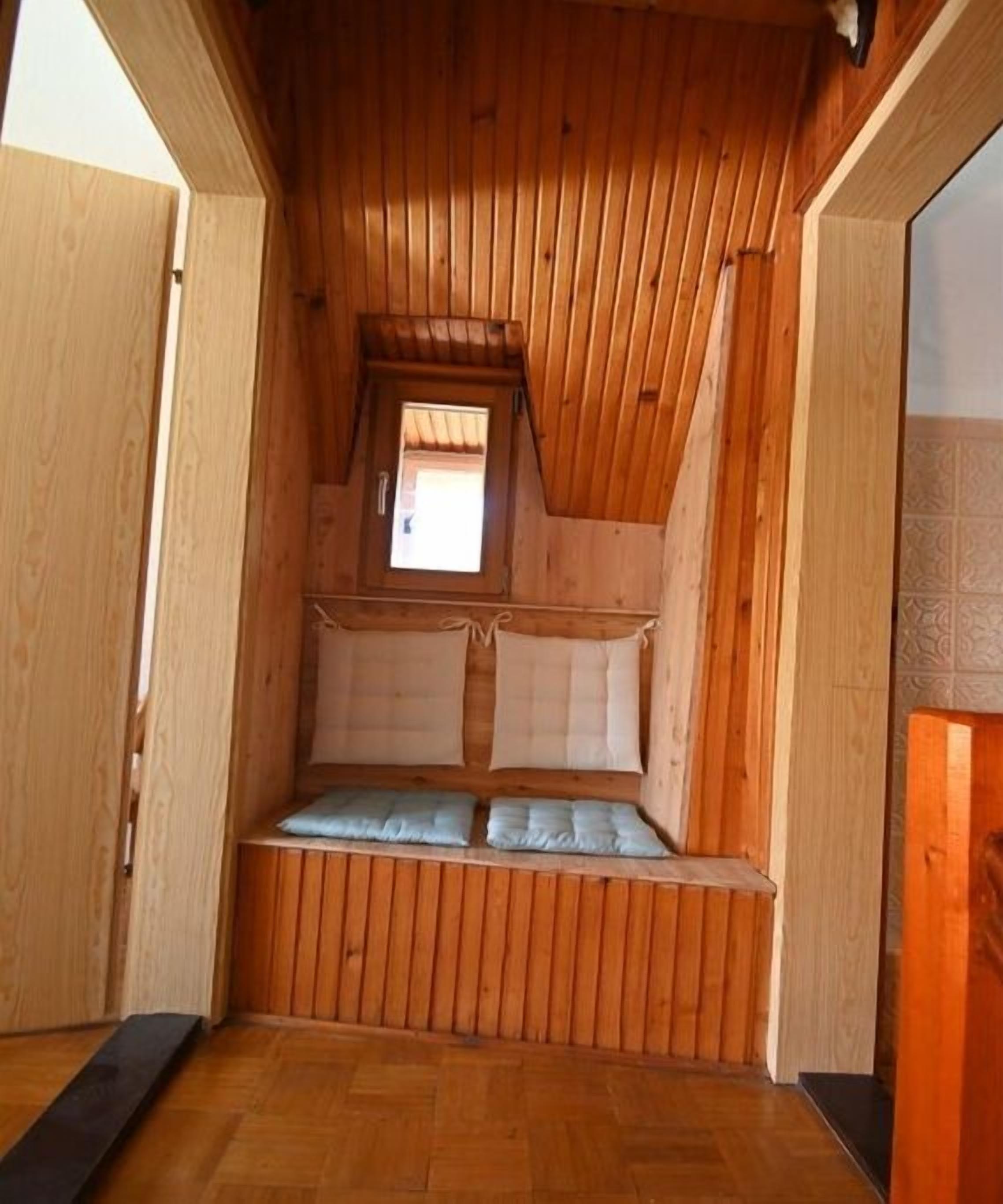 Un interior de madera con techo inclinado, una ventana pequeña y un banco con cojines.
