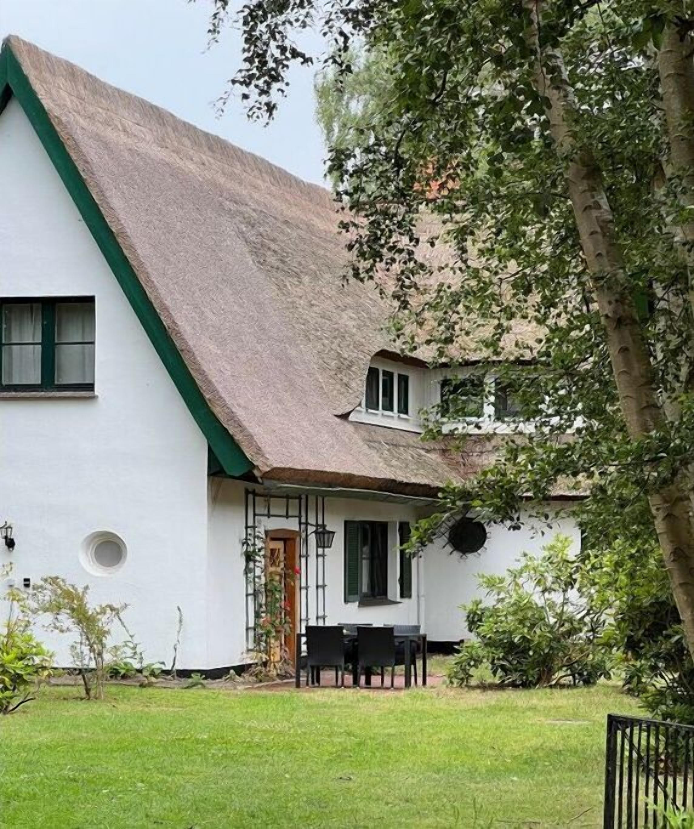 Un edificio blanco con techo verde y un pequeño jardín con mesa y sillas.