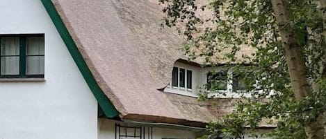 Un edificio blanco con techo verde y un pequeño jardín con mesa y sillas.