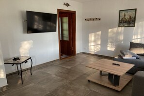 Ein Wohnzimmer mit Flachbildfernseher, Holztisch, Sofa und einem kleinen Tisch mit Fernbedienung.