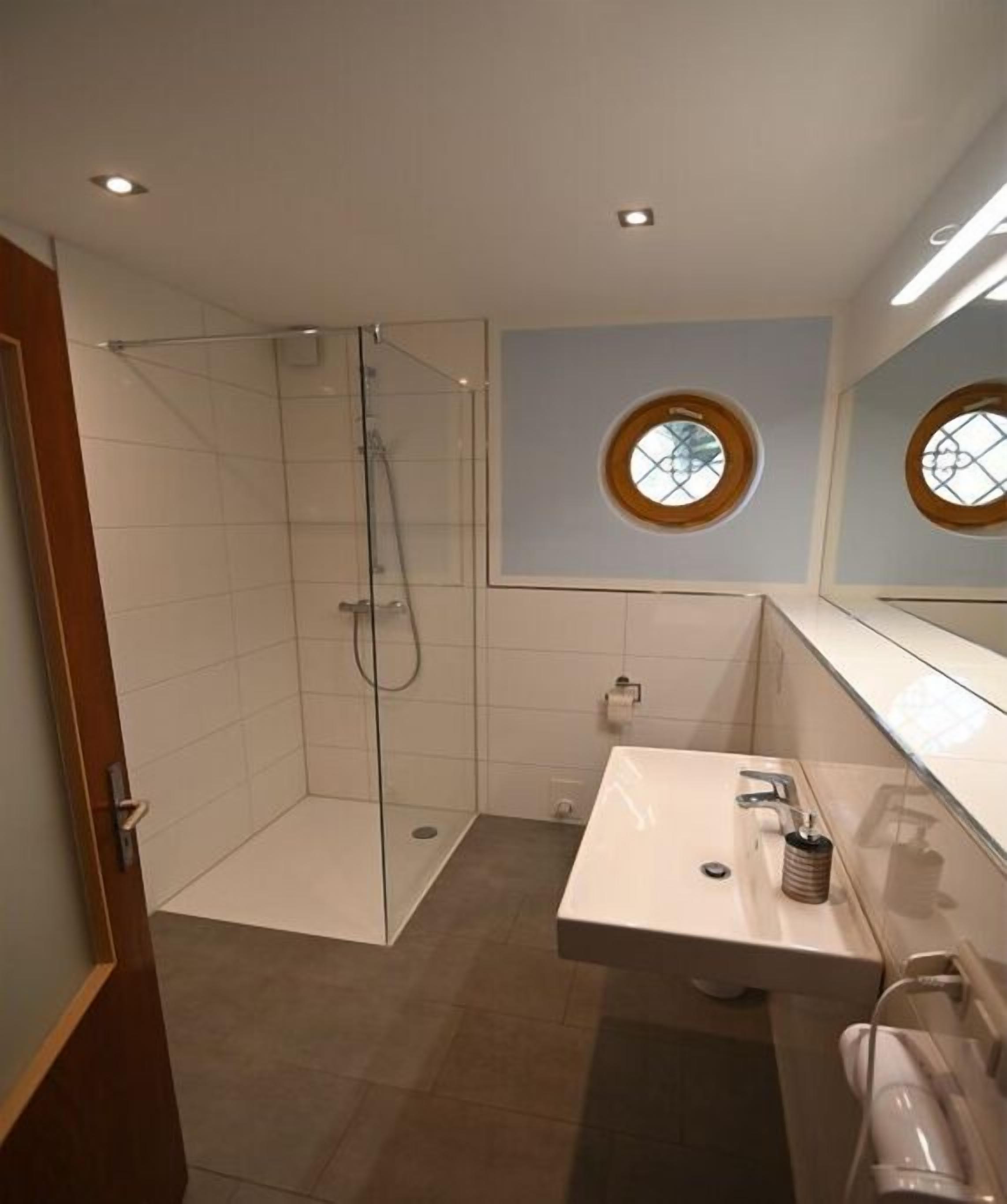 Un baño moderno con cabina de ducha acristalada, lavamanos con espejo y ventana con marco de madera.