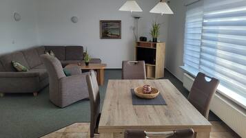 A modern living room with a sofa, a dining table with chairs, a coffee table, a floor lamp, and a window with blinds.
