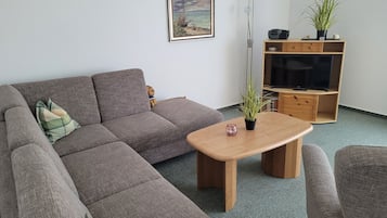 A living room with a sectional sofa, a wooden coffee table, a TV stand, and a floor lamp.