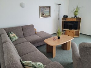 Een woonkamer met een hoekbank, een houten salontafel, een tv-meubel en een vloerlamp.