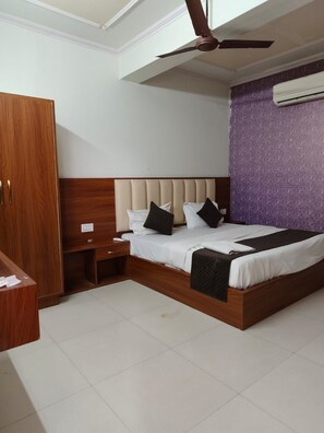 A bedroom with a bed, a wardrobe, a nightstand, a ceiling fan, and an air conditioning unit. - Hotal prime stay  (Jaipur)