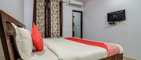 A bedroom with a bed, curtains, an air conditioning unit, a television, and a door.