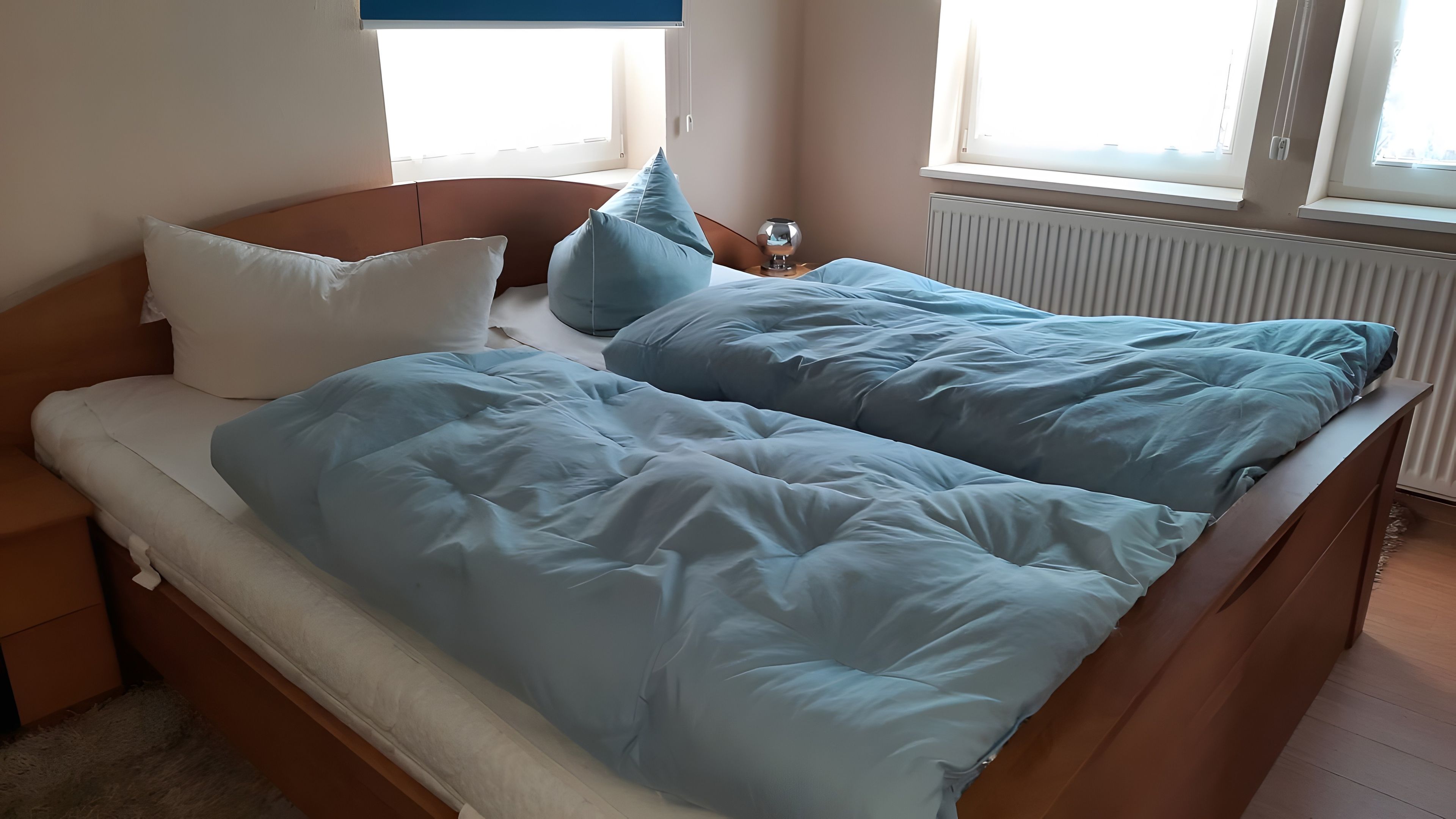Ein Bett mit einem hölzernen Kopfteil, einem weißen Kopfkissen und einer blauen Decke.