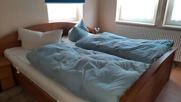 Ein Bett mit einem hölzernen Kopfteil, einem weißen Kopfkissen und einer blauen Decke.