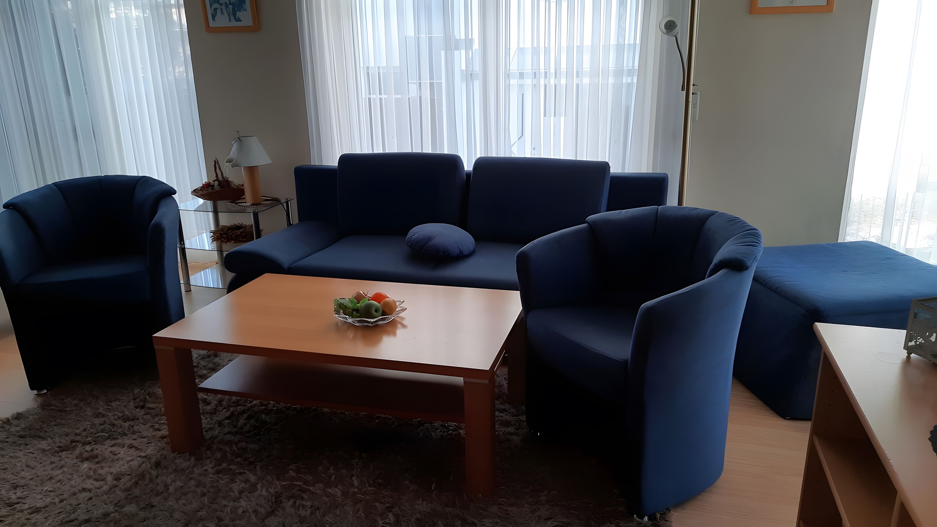 Una sala de estar moderna con un sofá azul, una mesa de centro de madera con fruta, y una mesita auxiliar de vidrio.