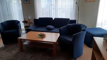 Una sala de estar moderna con un sofá azul, una mesa de centro de madera con fruta, y una mesita auxiliar de vidrio.