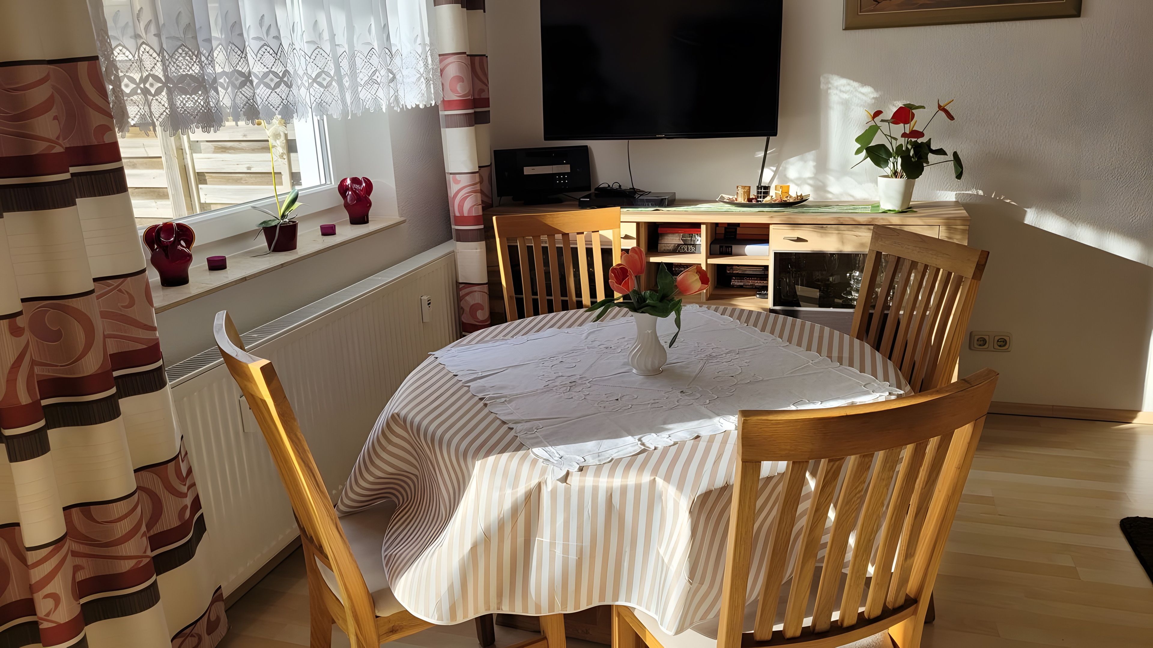 Ein Essbereich mit einem runden Tisch, Stühlen, einem Fernseher und einem Fenster mit Vorhängen.