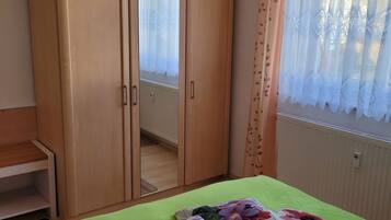 Ein Zimmer mit Kleiderschrank, einem Bett mit grüner Bettdecke und einem Fenster mit Spitzenvorhängen.