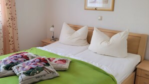 Un llit ben arreglat amb llençols blancs i dos coixins, una manta de color verd i dos coixins decoratius amb motius florals.