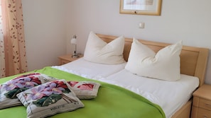 Ein ordentlich bezogenes Bett mit weißen Bettwäsche, zwei Kissen, einer grünen Tagesdecke und zwei dekorativen Kissen mit floralem Muster.