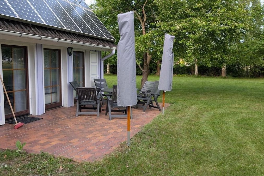 A house with a solar panel roof, a covered patio with chairs, and a lawn.