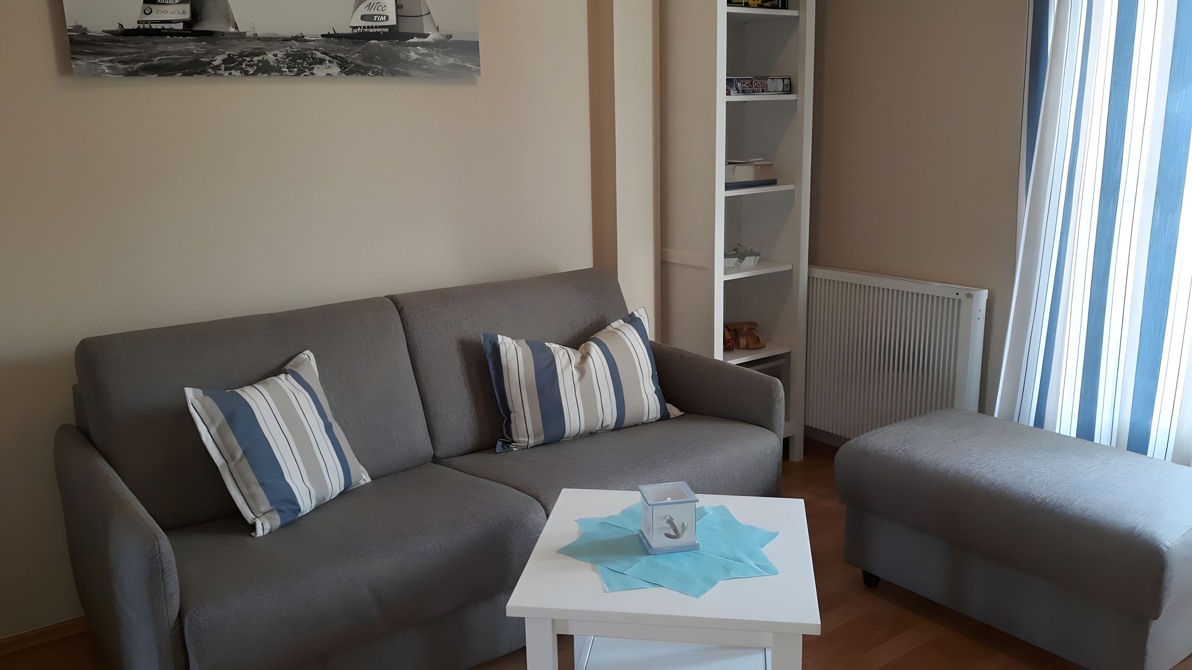 Ein Wohnzimmer mit einem grauen Sofa, einem passenden Sessel, einem kleinen weißen Tisch mit einem dekorativen Gegenstand und einem Bücherregal.