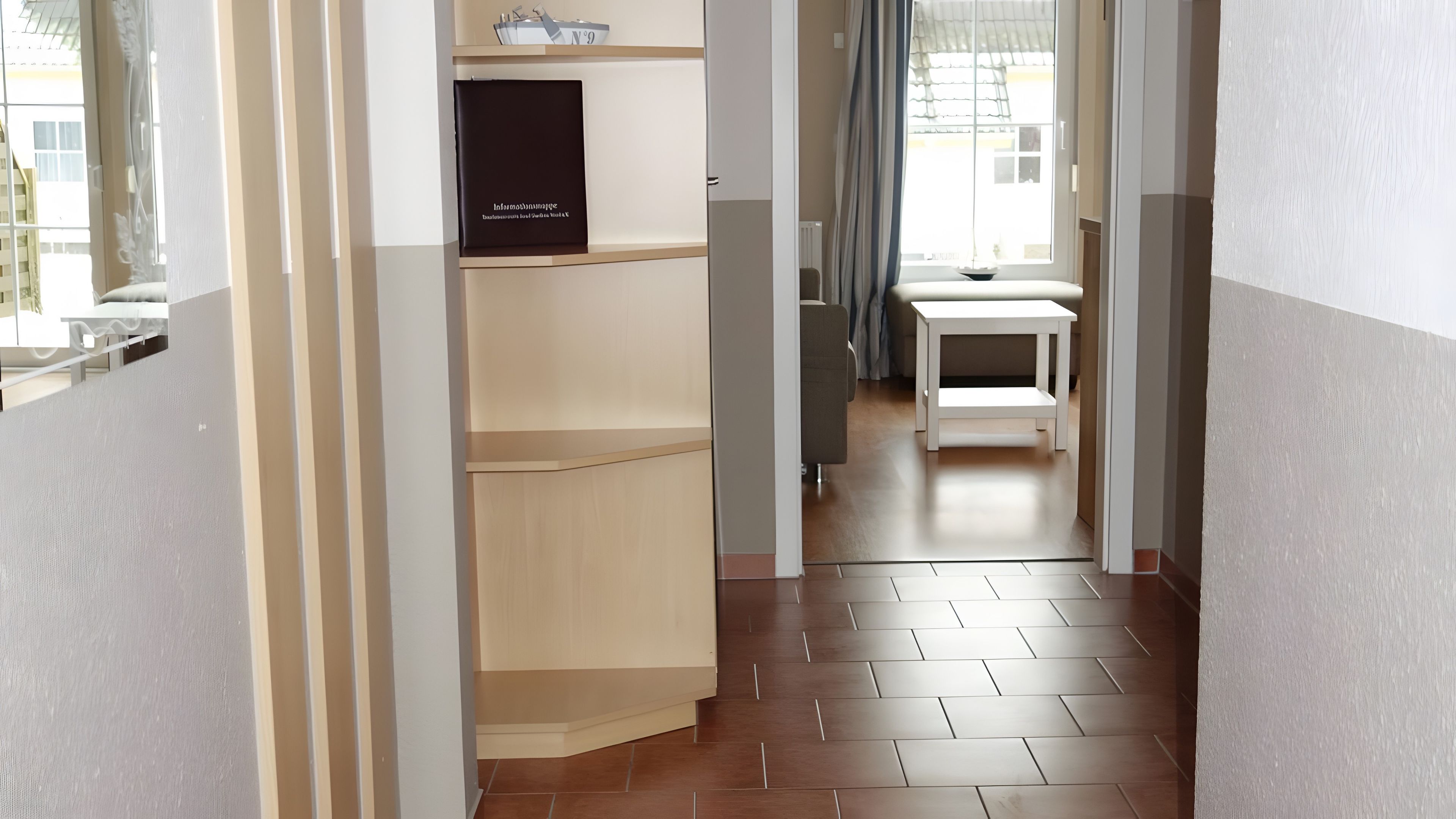 A hallway with a wooden floor, a white table, and a shelf with a black box.