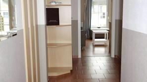A hallway with a wooden floor, a white table, and a shelf with a black box. - Apartment 'Koserow, Förster-Schrödter-Straße' with Terrace and Wi-Fi (Koserow)