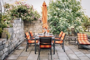 Eine Terrasse im Freien mit einer Steinmauer, einem Esstisch und Lounge-Stühlen.